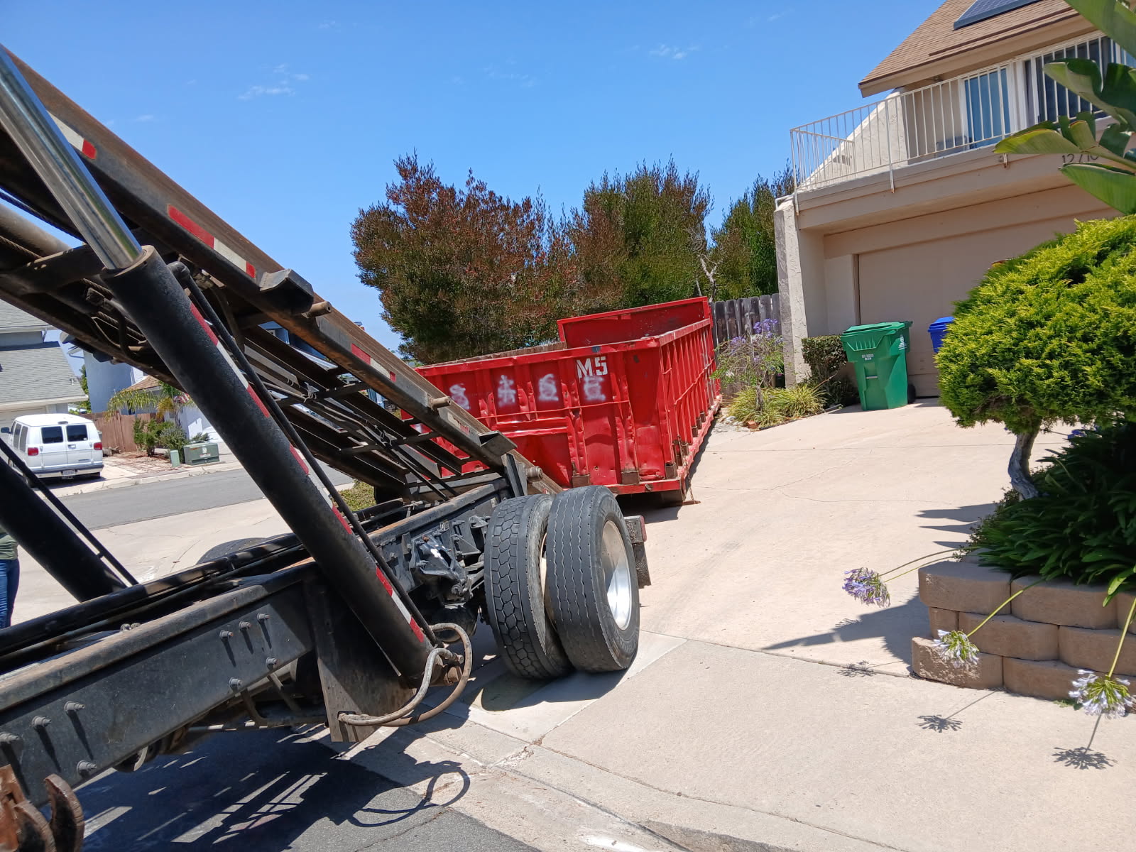 Red 20-yard roll-off dumpster being delivered to a Clairemont driveway with a hauling truck rolling it off