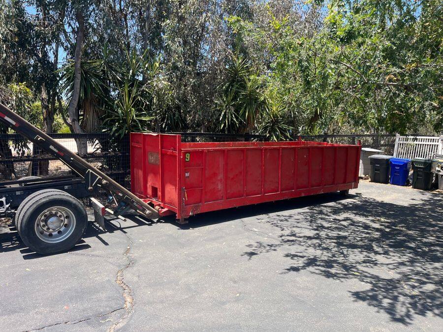 25-yard red roll-off dumpster placed on a North County driveway under eucalyptus trees